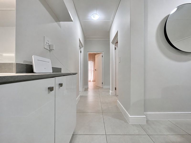A clean, modern hallway featuring neutral tiled flooring, built-in cabinetry with stone countertops, and crisp white finishes throughout.