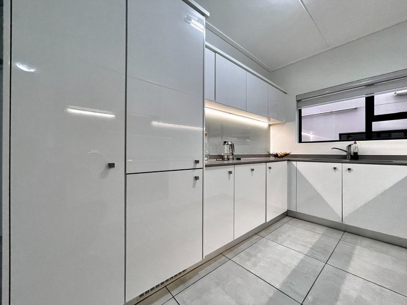 Modern kitchen featuring sleek white high-gloss cabinetry, stone countertops, under-cabinet lighting, and large format floor tiles.