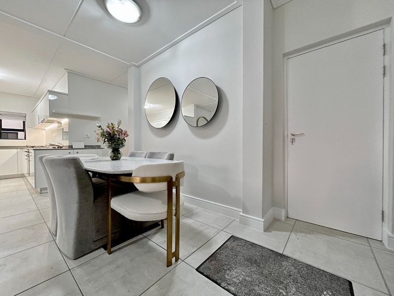 An open-plan living and dining area featuring tiled flooring, neutral walls, and a modern kitchen with built-in cabinetry.