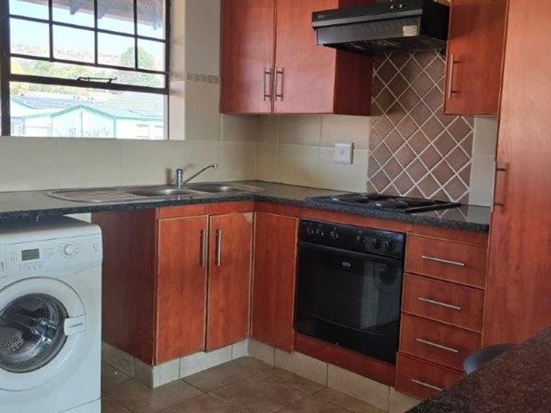 A functional kitchen featuring wooden cabinetry, granite countertops, built-in oven, hob, extractor fan, and space for a washing machine.