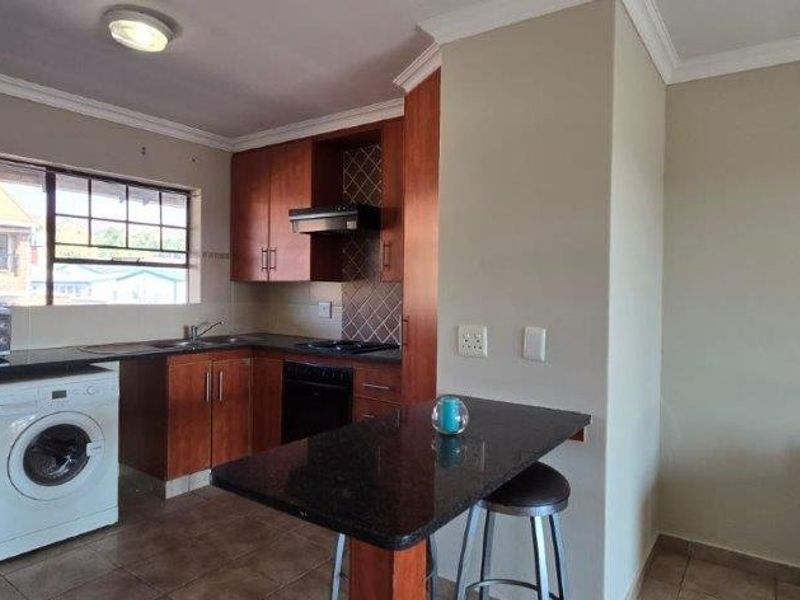 Open-plan kitchen featuring wood-finish cabinetry, granite countertops, built-in oven, extractor fan, and a breakfast bar, seamlessly integrated with the living area.