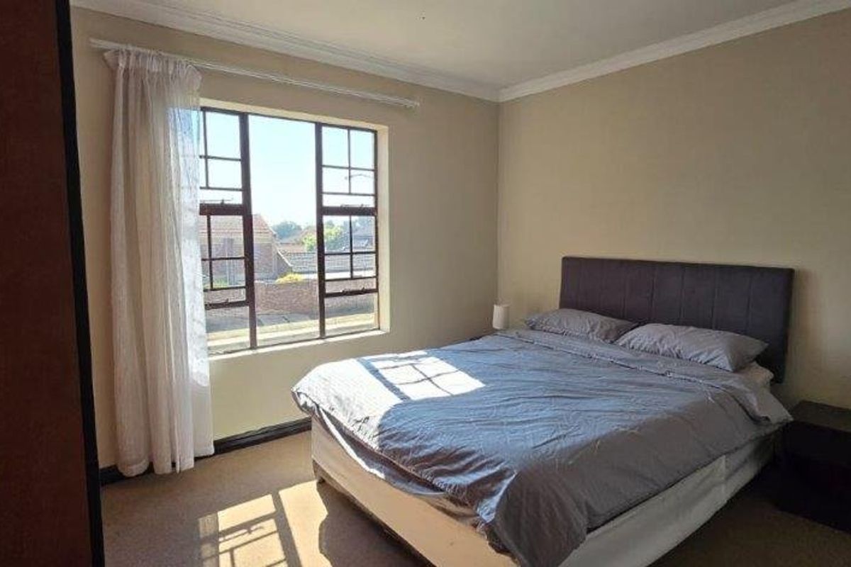 A well-lit bedroom featuring neutral wall tones, carpeted flooring, and a large window allowing for natural light.
