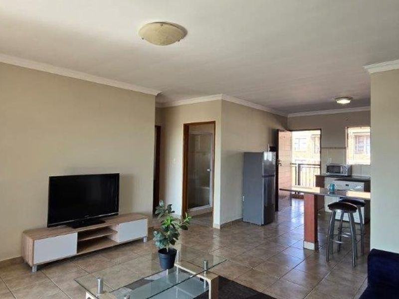 Open-plan living and kitchen area featuring tiled flooring, neutral wall tones, and a functional breakfast bar layout.