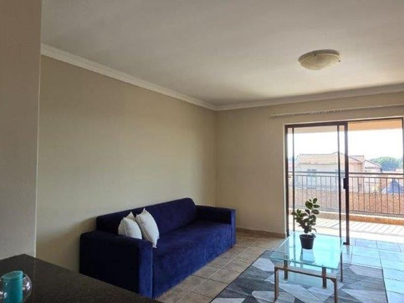 A living room featuring tiled flooring, neutral walls, and a sliding glass door providing access to an outdoor balcony area.
