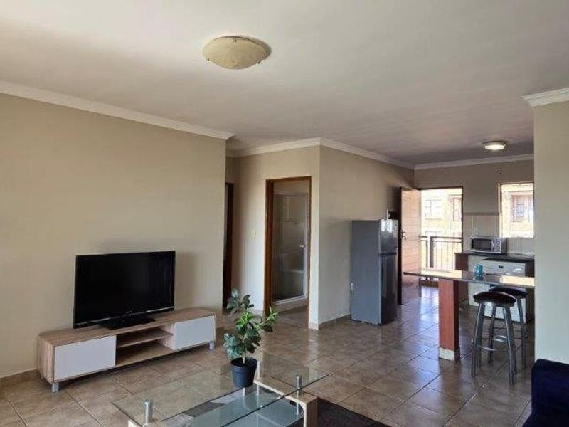 Open-plan living area featuring tiled flooring, a breakfast counter, and a functional kitchen layout, providing a versatile space for dining and relaxation.
