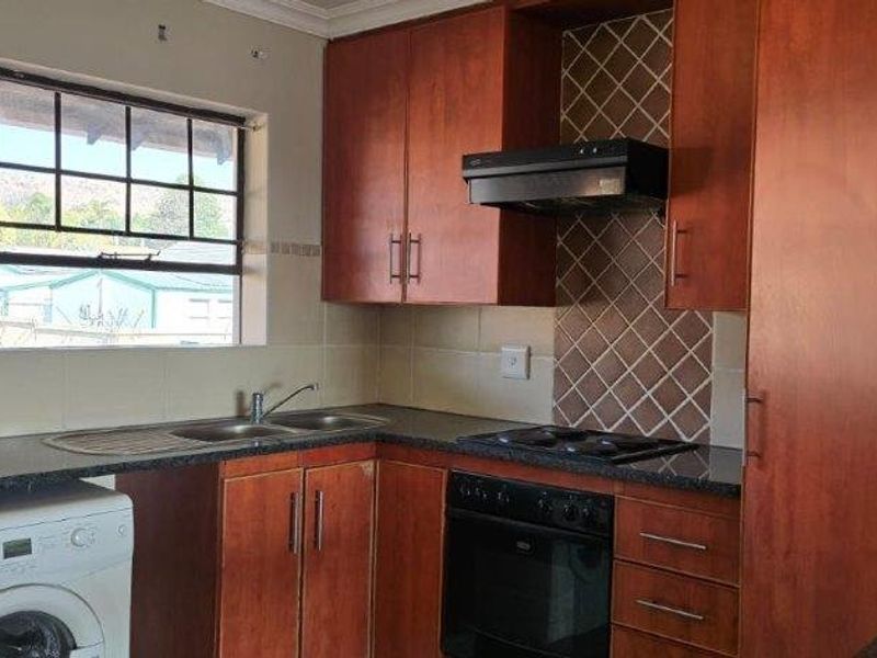 A functional kitchen featuring wood-finish cabinetry, dark laminate countertops, a built-in oven with hob, and a tiled backsplash with a window view.