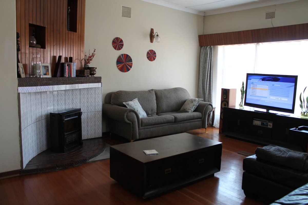 A living room featuring timber flooring, a fireplace with decorative tiling, and timber wall paneling, offering a traditional layout.