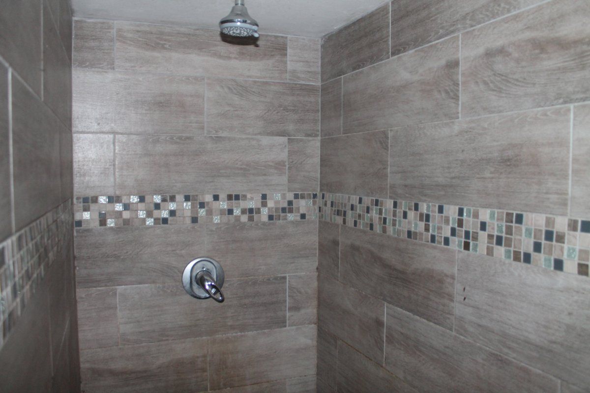 A shower enclosure featuring wood-look ceramic wall tiles and a decorative mosaic accent border with a standard shower mixer and head.