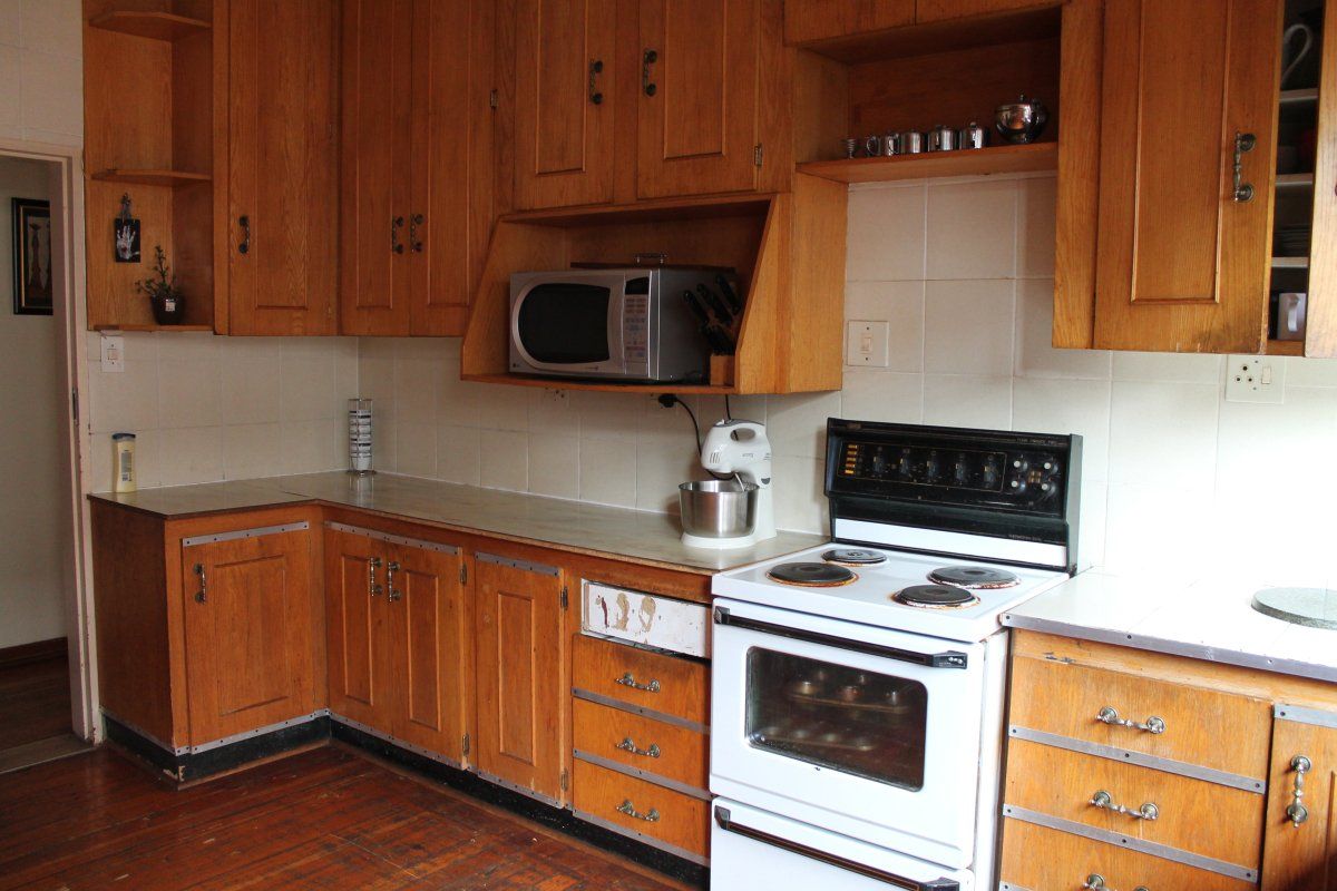 A dated kitchen featuring original wooden cabinetry, tiled backsplash, and a freestanding electric stove, offering significant potential for a modern renovation.