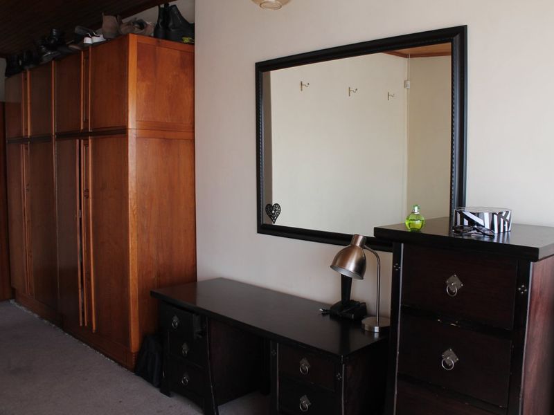 A bedroom featuring a large built-in wooden wardrobe and carpeted flooring, providing ample storage space.