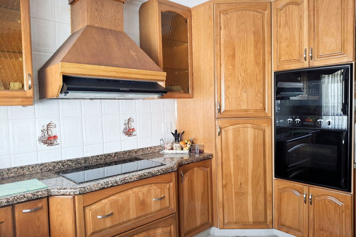 A functional kitchen featuring traditional wooden cabinetry, granite countertops, a built-in oven, and an integrated extractor fan with a tiled backsplash.