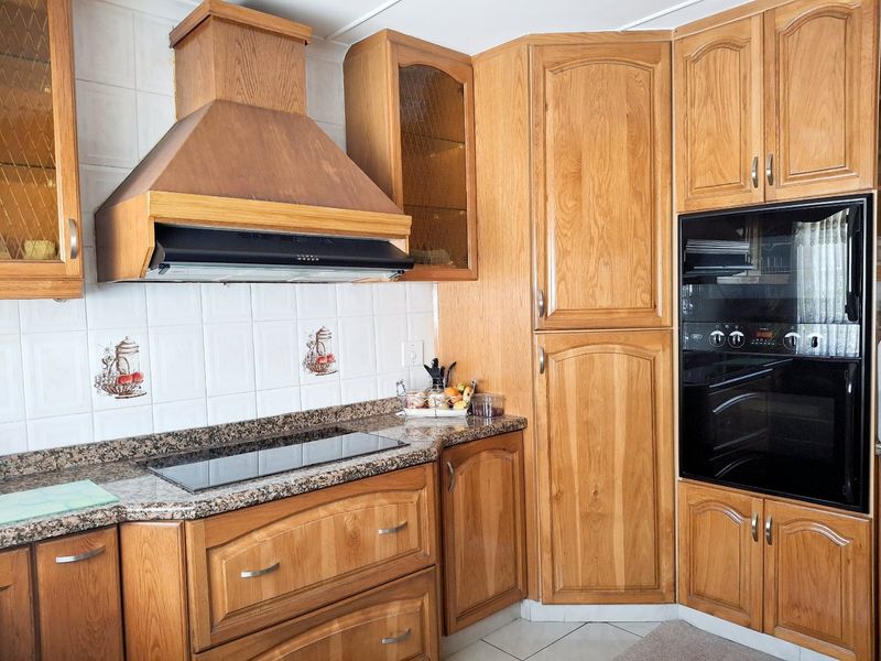 A functional kitchen featuring traditional wooden cabinetry, granite countertops, a built-in oven, and an integrated extractor fan with a tiled backsplash.