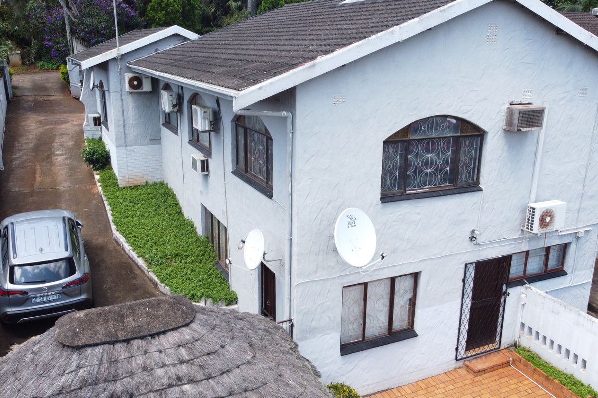 Aerial view of the rear exterior of the house, featuring a tiled roof, multiple air conditioning units, security gates, and a paved driveway.