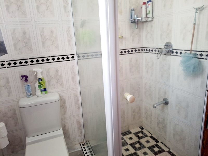 A functional bathroom featuring a shower enclosure with tiled walls and flooring, complemented by a standard toilet and chrome shower fixtures.
