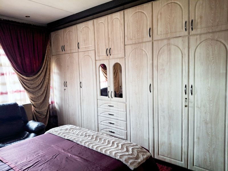 Bedroom featuring extensive floor-to-ceiling built-in wooden cupboards with integrated drawers and a central mirrored vanity section.