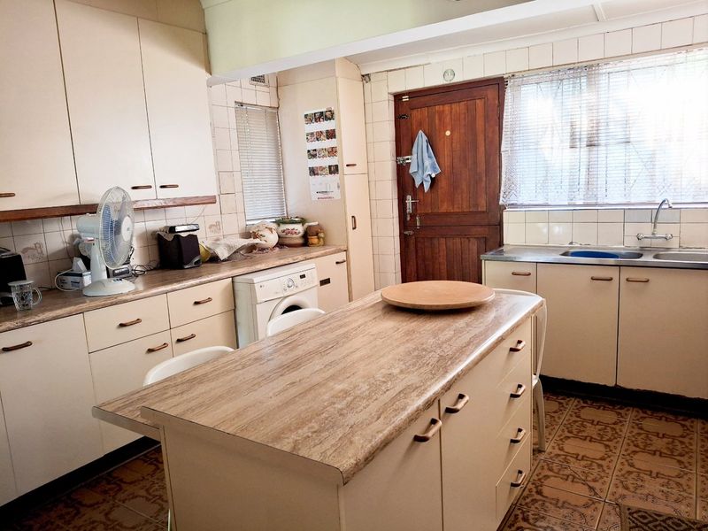 A functional kitchen featuring dated cabinetry, laminate countertops, tiled backsplash, and a central island, offering potential for a modern renovation.