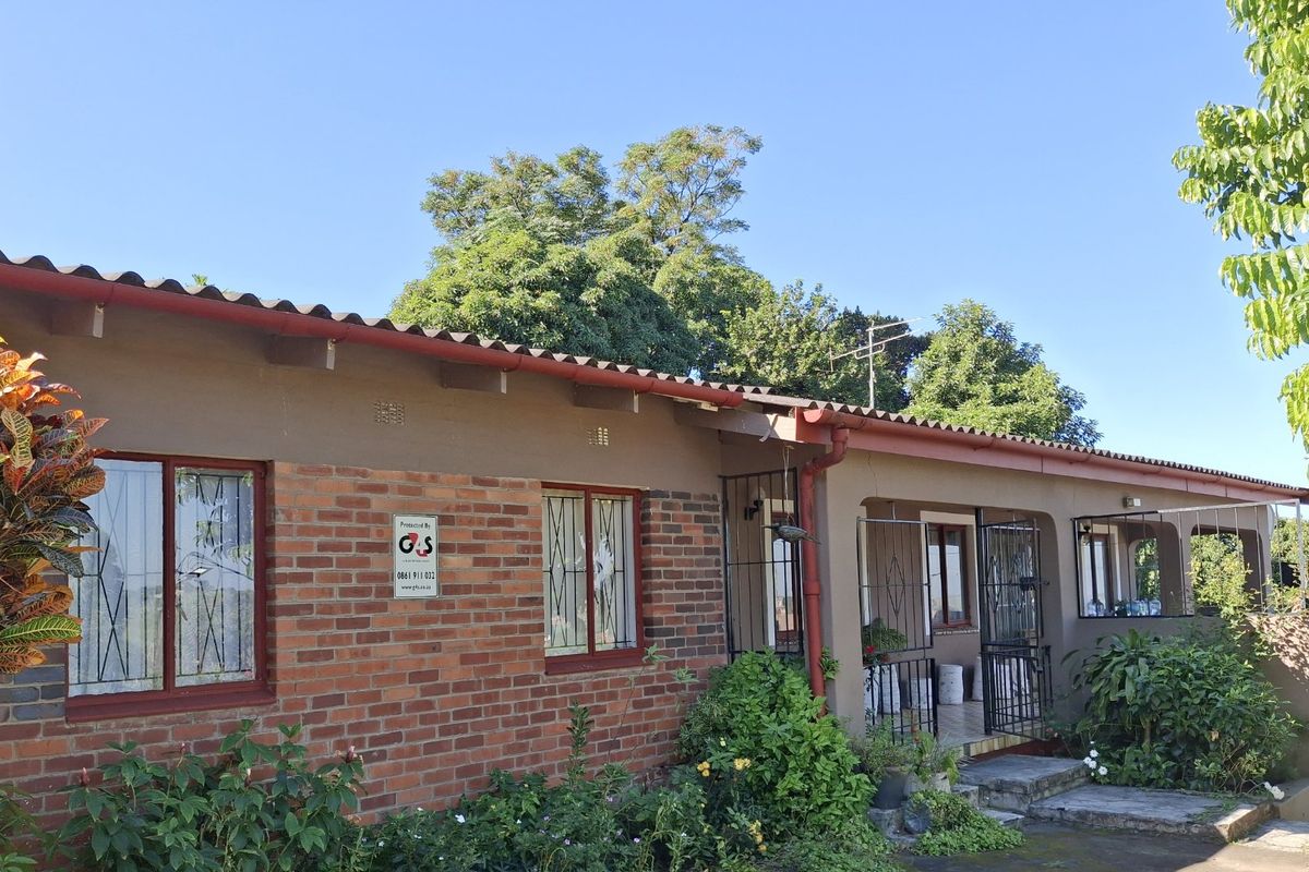 Rear elevation of a single-story brick house featuring a covered patio area, security bars on windows, and established garden surroundings.