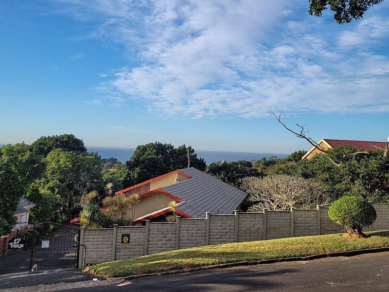 A street-level view of the property entrance, featuring a secure boundary wall, gated access, and a view of the surrounding residential landscape.