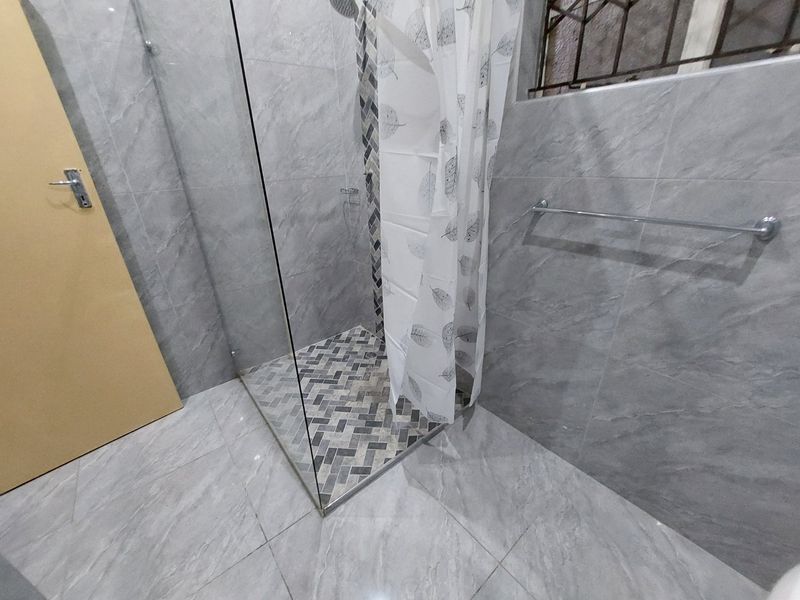 A modern bathroom featuring grey marble-look wall and floor tiles, a glass shower enclosure with a decorative mosaic accent strip, and a chrome towel rail.