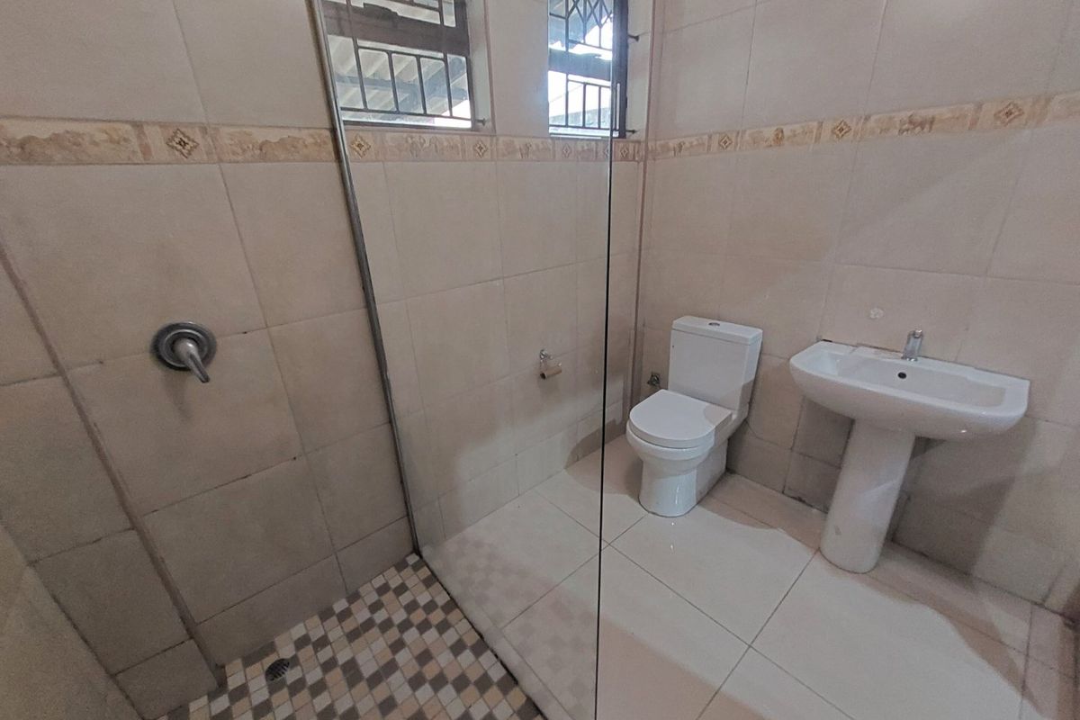 A functional bathroom featuring a pedestal basin, toilet, and a glass-enclosed shower with tiled finishes throughout.
