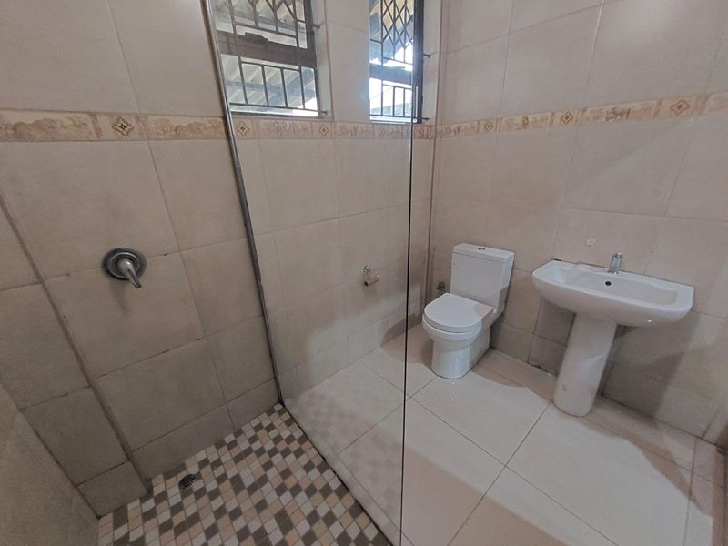 A functional bathroom featuring a pedestal basin, toilet, and a glass-enclosed shower with tiled finishes throughout.