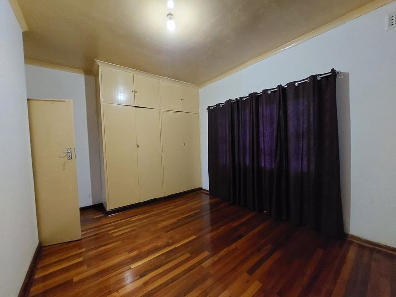A spacious bedroom featuring polished hardwood flooring, built-in storage cupboards, and neutral wall finishes, offering a blank canvas for personalization.