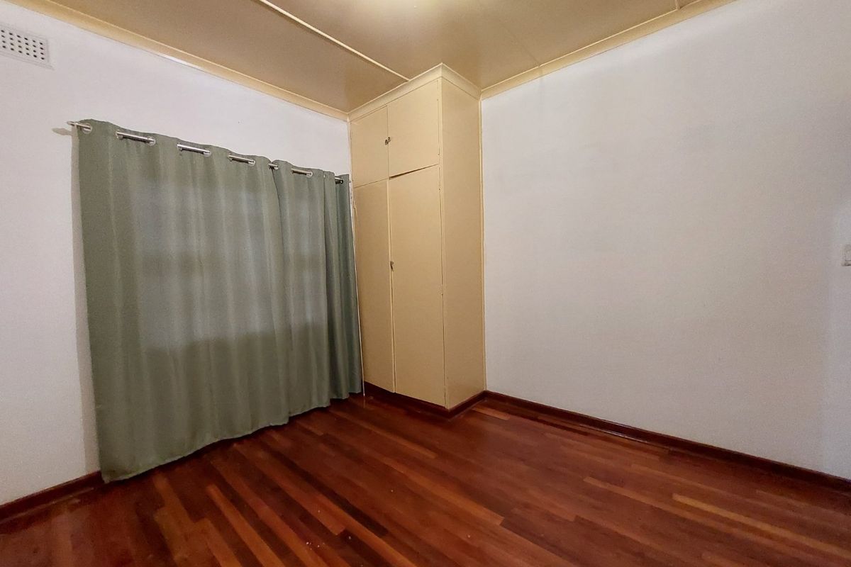 A vacant bedroom featuring polished hardwood flooring, a built-in wardrobe, and neutral wall finishes, offering a clean canvas for personalization.