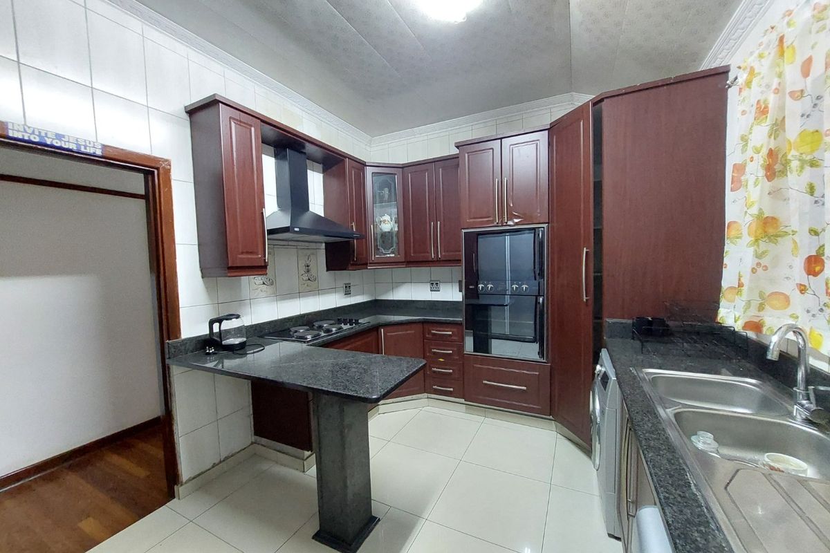 A functional kitchen featuring dark wood cabinetry, granite countertops, a built-in oven, extractor fan, and double sink with tiled finishes.