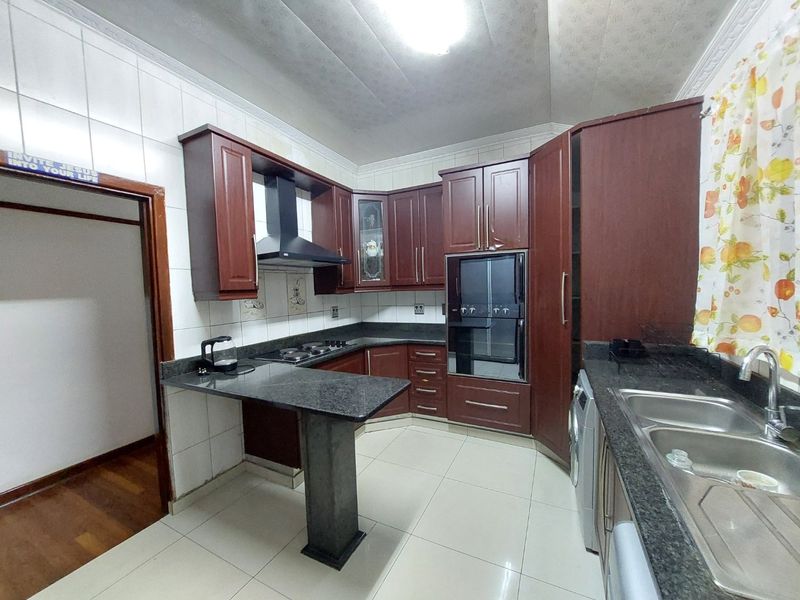 A functional kitchen featuring dark wood cabinetry, granite countertops, a built-in oven, extractor fan, and double sink with tiled finishes.