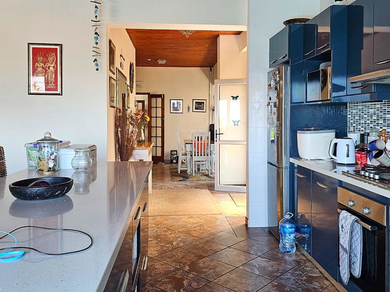 Open-plan kitchen featuring modern blue cabinetry, quartz countertops, and a mosaic backsplash, flowing into an adjacent dining area with timber ceiling accents.