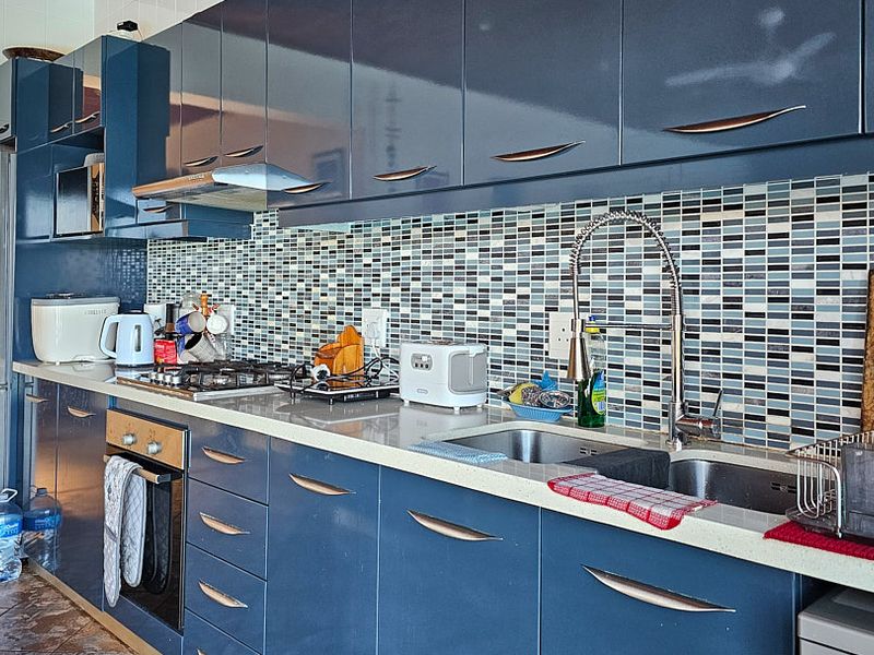 Modern kitchen featuring high-gloss blue cabinetry, stone countertops, a mosaic tile backsplash, and integrated stainless steel appliances.