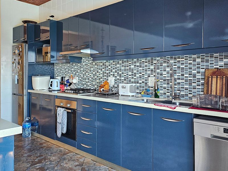 Modern kitchen featuring glossy blue cabinetry, a mosaic tile backsplash, stone countertops, and integrated stainless steel appliances.