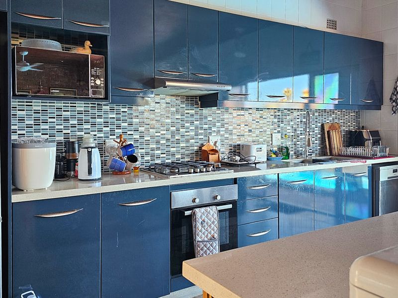 Modern kitchen featuring high-gloss blue cabinetry, a mosaic tile backsplash, stone countertops, and integrated stainless steel appliances.