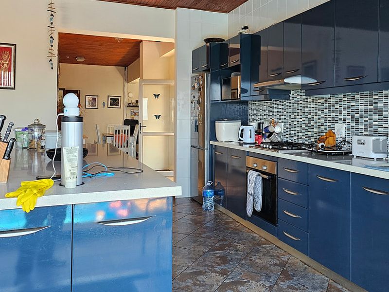 Modern kitchen featuring dark blue cabinetry, stone countertops, a mosaic tile backsplash, and a functional kitchen island, providing ample workspace and storage.