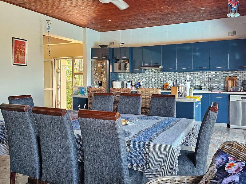 Open plan kitchen and dining area featuring blue cabinetry, mosaic backsplash, timber ceiling, and sliding doors leading to the outdoor space.