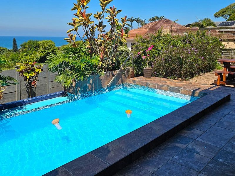 Outdoor pool area featuring a tiled swimming pool with mosaic accents, paved surround, and scenic ocean views in a landscaped garden setting.