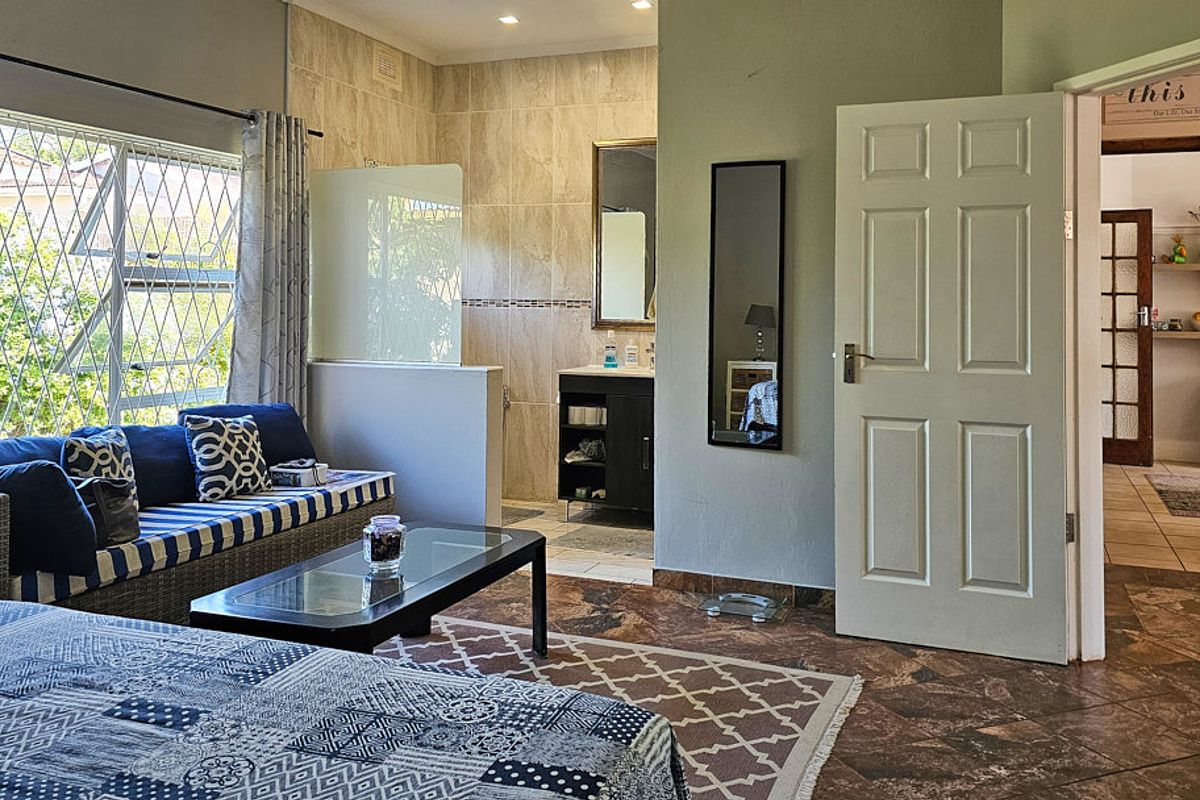 Spacious bedroom featuring tiled flooring, an open-plan en-suite bathroom with a vanity, and large windows with security bars.