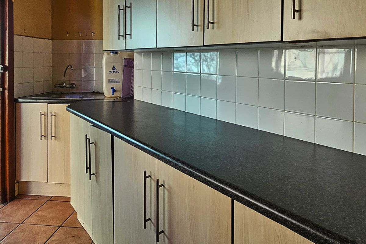 A functional kitchen area featuring laminate cabinetry, dark countertops, a tiled backsplash, and a stainless steel sink with direct outdoor access.