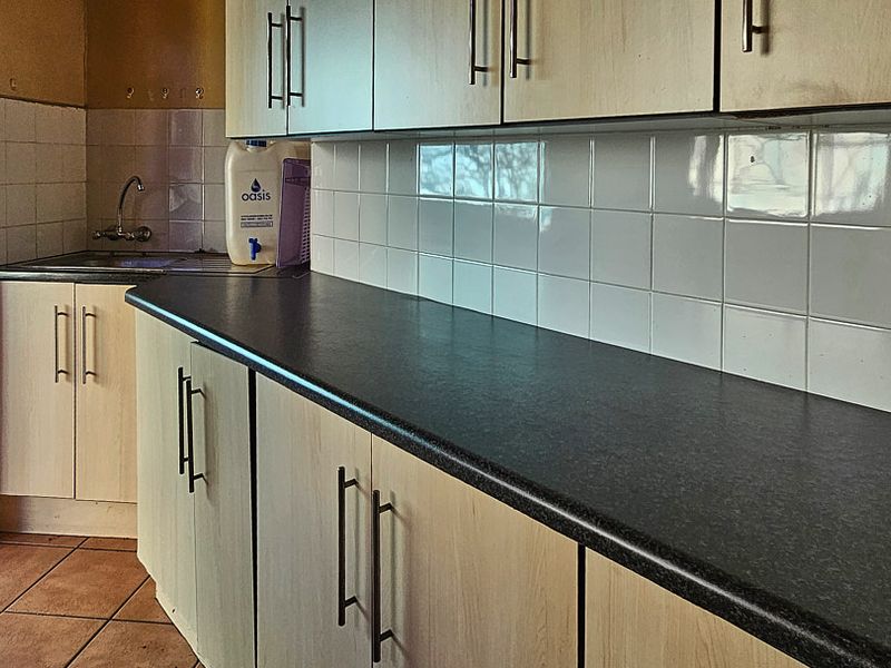 A functional kitchen area featuring laminate cabinetry, dark countertops, a tiled backsplash, and a stainless steel sink with direct outdoor access.