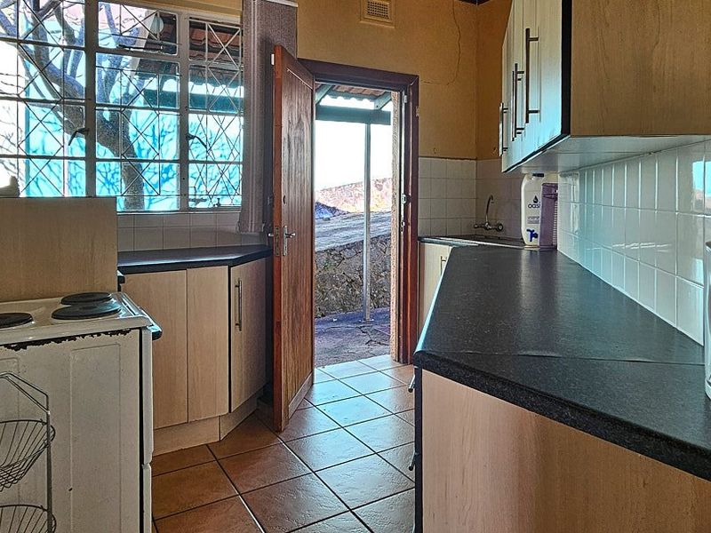 A functional kitchen featuring tiled flooring, laminate countertops, and built-in cabinetry, with direct access to an outdoor area.