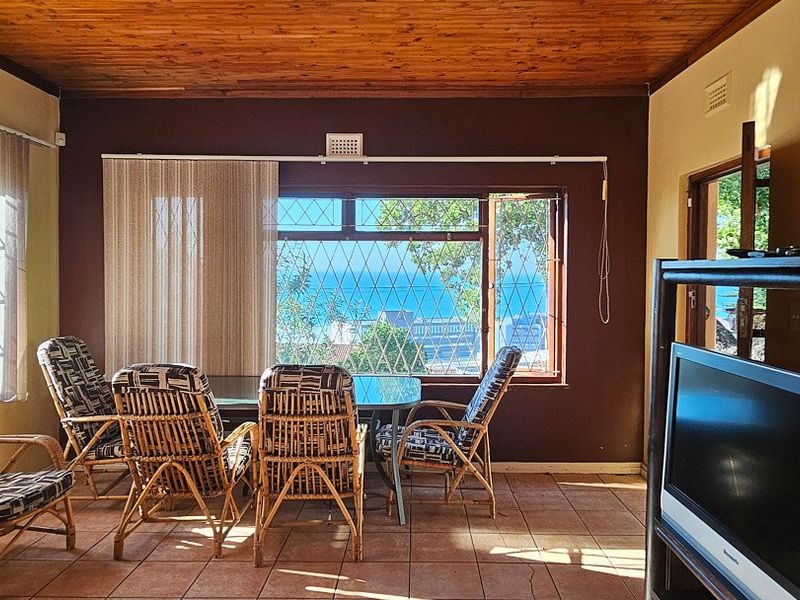 Living area featuring a timber ceiling, tiled flooring, and large windows with security bars, offering a view of the ocean.