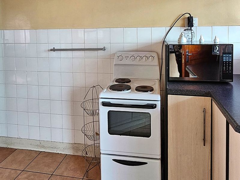 A functional kitchen area featuring a freestanding electric stove, tiled splashback, and laminate cabinetry with dark countertops.