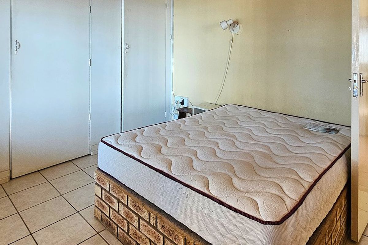 A bedroom featuring built-in cupboards, tiled flooring, and a wall-mounted light fixture. The space requires cosmetic updates to improve its overall appeal.