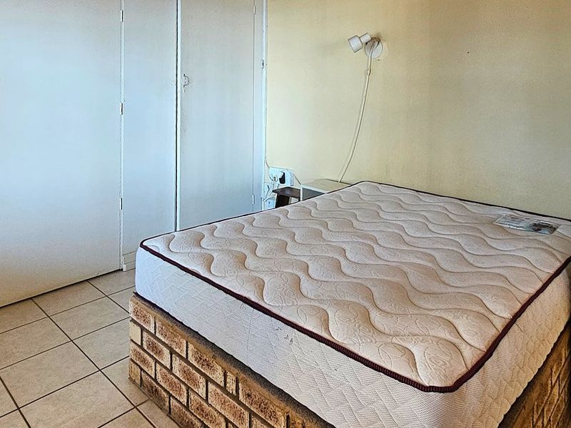 A bedroom featuring built-in cupboards, tiled flooring, and a wall-mounted light fixture. The space requires cosmetic updates to improve its overall appeal.