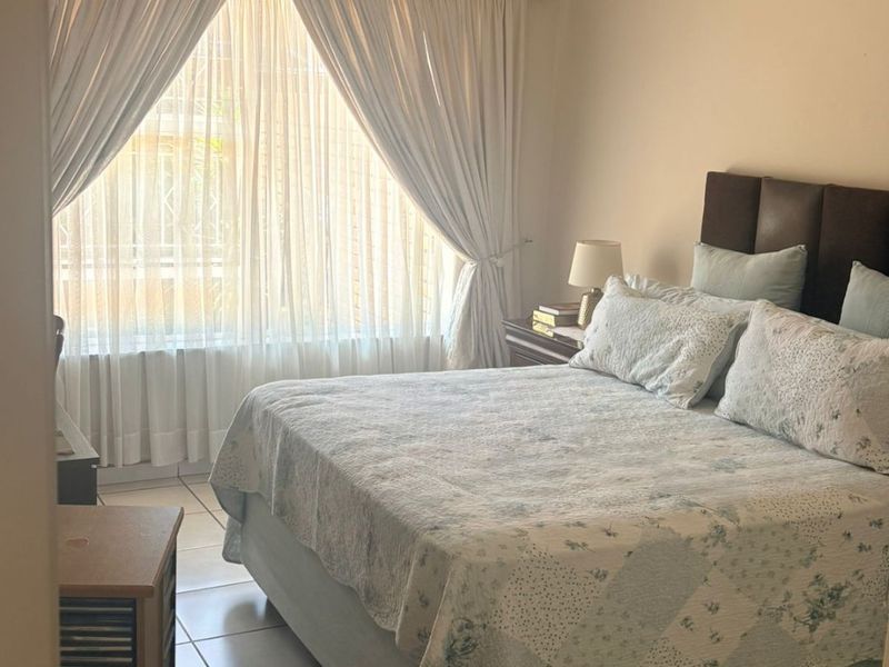 A well-lit bedroom featuring tiled flooring, a ceiling fan, and large windows with curtain rails, offering a comfortable and functional living space.