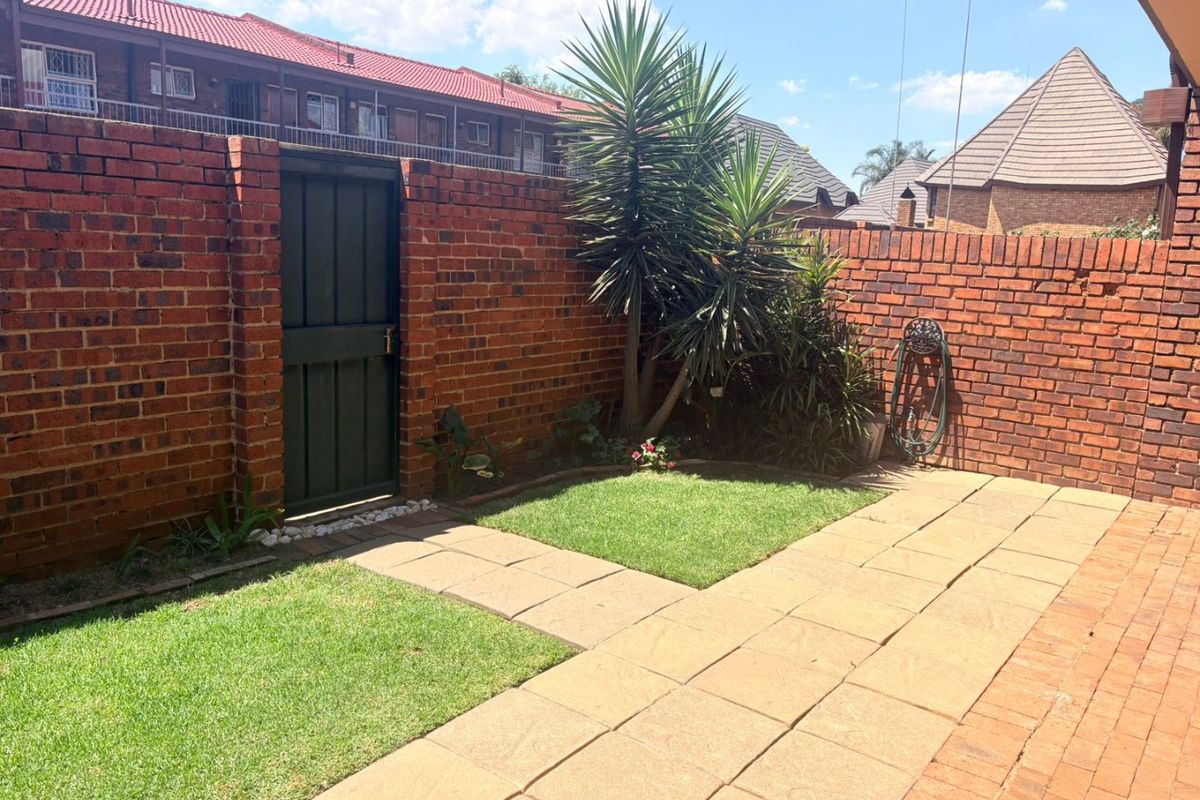 A private rear courtyard featuring a paved patio area, a small lawn, and a secure brick boundary wall with a pedestrian gate.