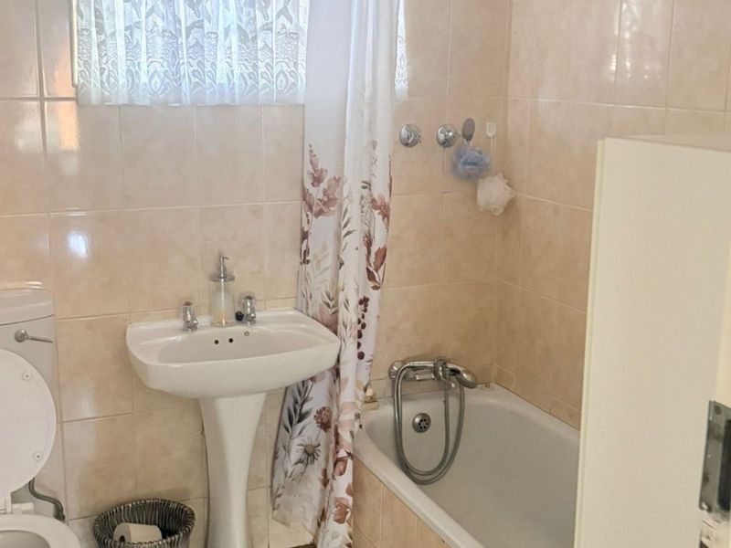 A functional bathroom featuring a pedestal basin, bathtub with shower head, and tiled finishes throughout.