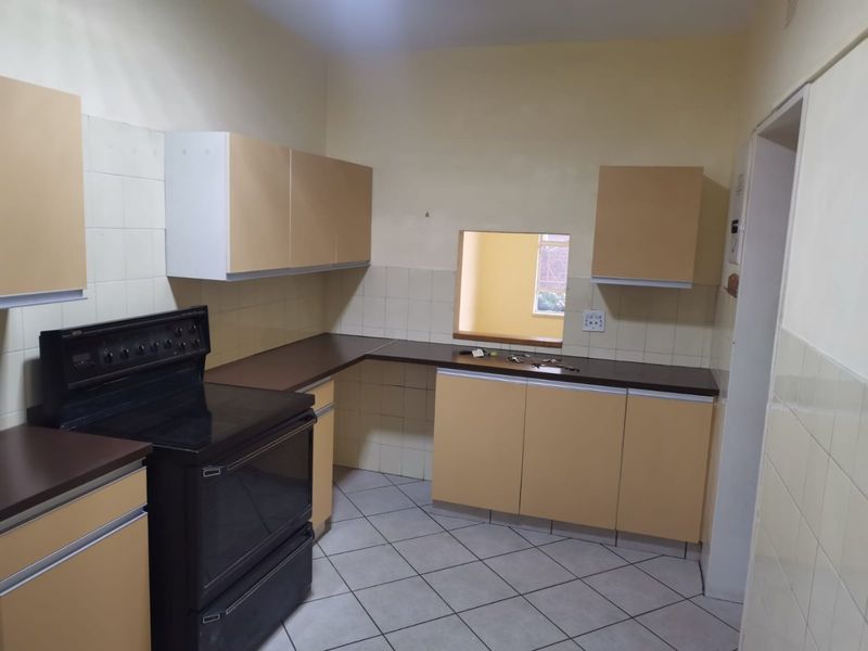 A functional kitchen featuring dated cabinetry, laminate countertops, a tiled backsplash, and a freestanding stove, with a convenient serving hatch to the adjacent room.
