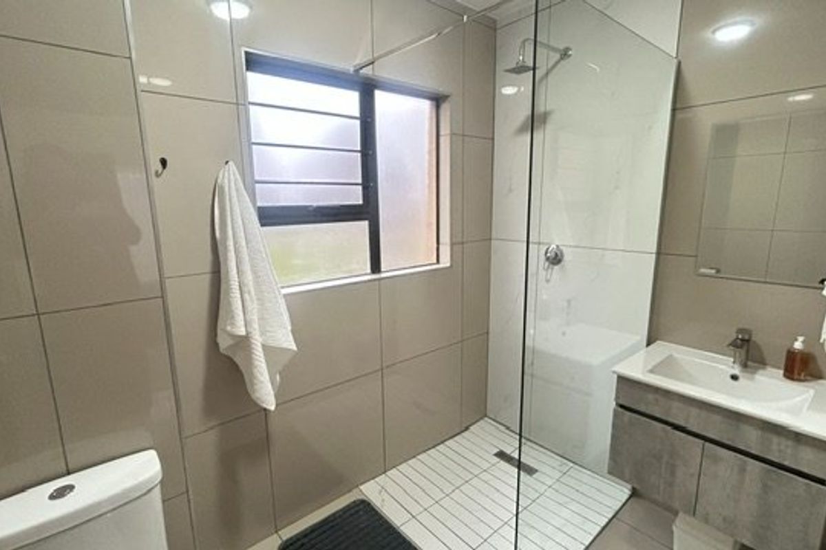 Modern bathroom featuring a walk-in shower with glass screen, wall-mounted vanity with basin, and neutral floor-to-ceiling wall tiling.