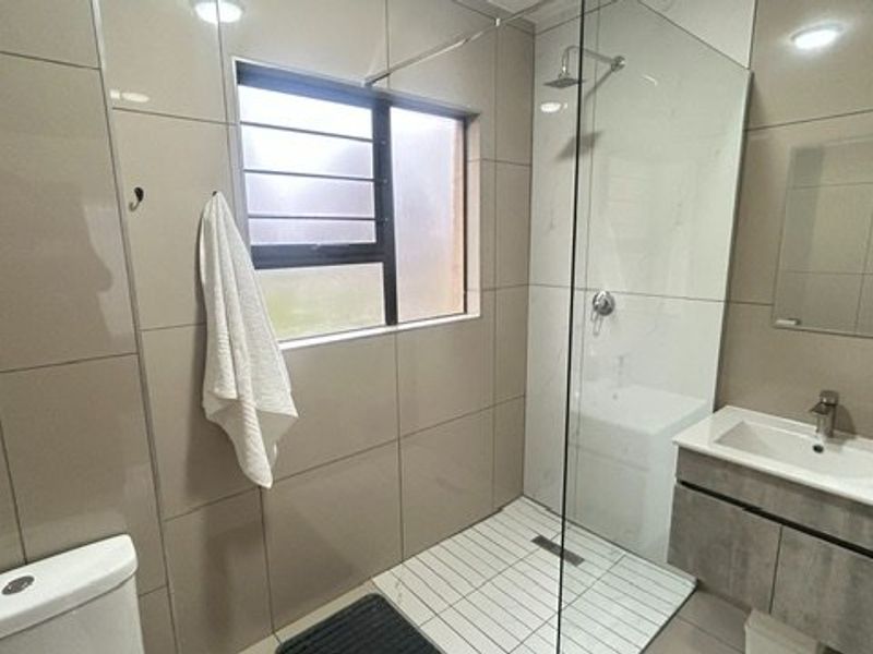 Modern bathroom featuring a walk-in shower with glass screen, wall-mounted vanity with basin, and neutral floor-to-ceiling wall tiling.